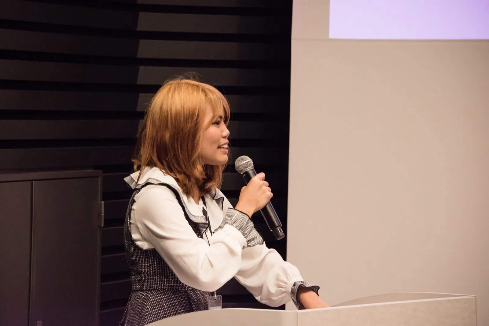 Ornida speaking into a microphone at a podium, hosting TSAJ Idea Day
